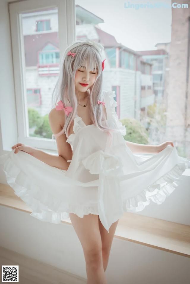 A woman in a white dress posing by a window.