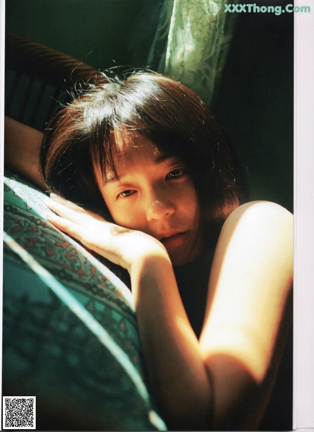 A young girl laying on a couch with her hand on her chin.