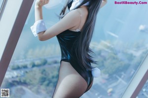 A woman in a black bodysuit posing in front of a window.