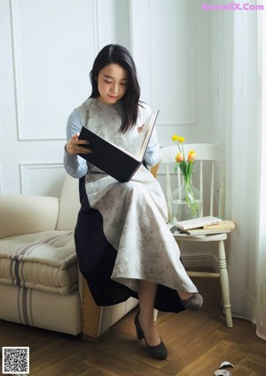 A woman sitting on the floor wearing a red skirt and black sweater.