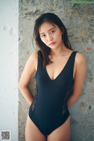 A woman leaning against a wall with a flower in her hand.