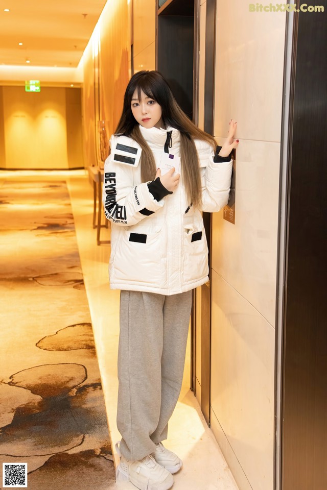 A woman leaning against a wall in a hallway.