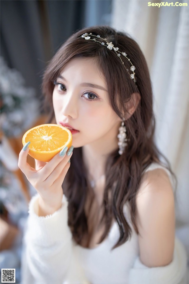 A woman holding an orange in front of her face.