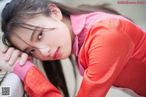 A young woman leaning against a fence with her hand on her chin.