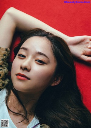 A young woman leaning against a curtain looking at the camera.