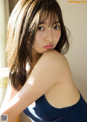 A woman in a blue tank top and tan panties crouching on the floor.