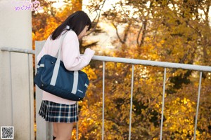 A woman in a pink sweater and plaid skirt walking down a road.