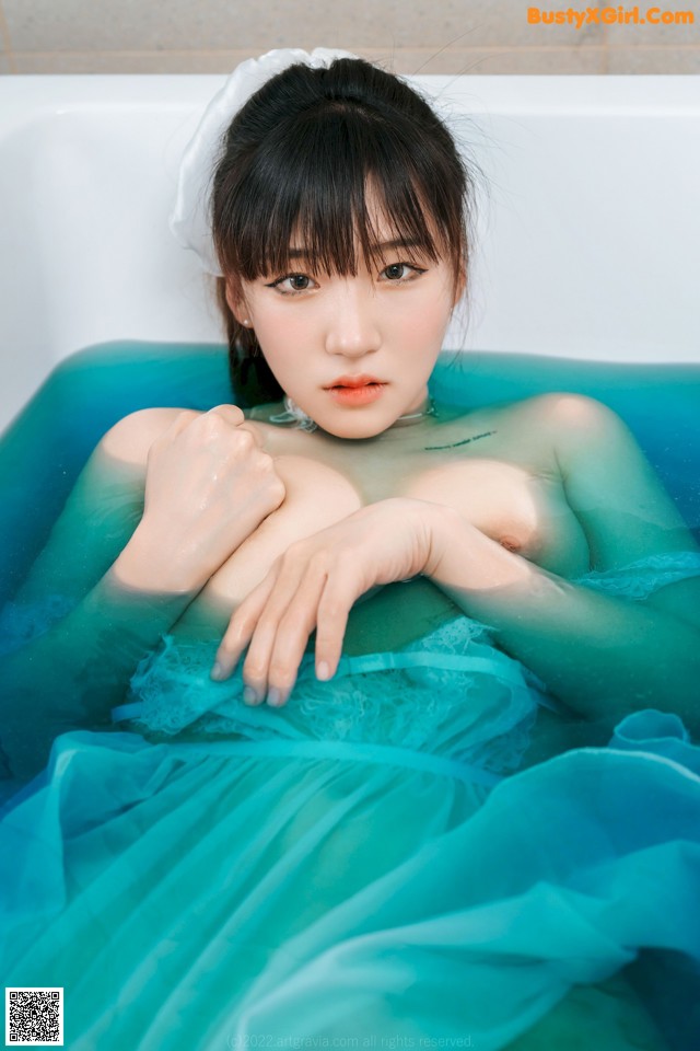 A woman in a blue dress sitting in a bathtub.