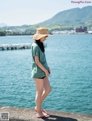 A young woman standing on a sidewalk next to a wall.
