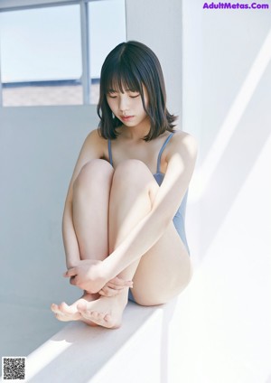 A woman in a blue bathing suit sitting on a ledge.