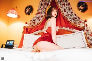 A woman sitting on a red chair in front of a red curtain.