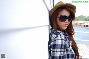 A woman in a plaid shirt and denim shorts posing on a bed.