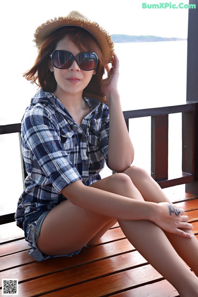 A woman sitting on a wooden bench wearing a hat and sunglasses.