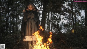 A woman sitting in front of a fire in the woods.