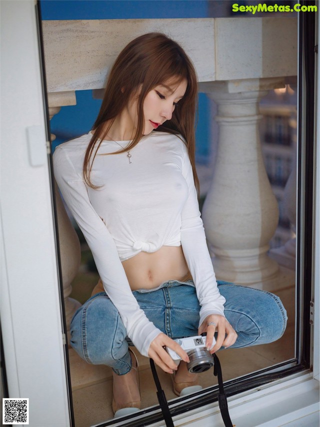 A woman sitting on a window sill holding a camera.