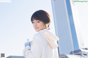 A woman in a white coat and black stockings sitting on a bench.