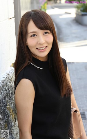 A woman in a black top and white skirt sitting on a bed.